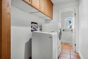 Laundry room featuring cabinets, light tile patterned floors, and washing machine and dryer