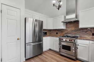 Kitchen featuring wall chimney exhaust hood, white cabinetry, appliances with stainless steel finishes, and light hardwood / wood-style flooring