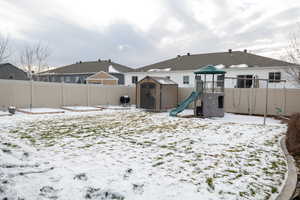 Snow covered house featuring a playground and a storage unit