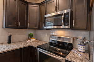 Kitchen featuring light stone countertops, dark brown cabinetry, backsplash, and appliances with stainless steel finishes