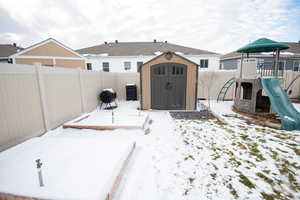 Snowy yard featuring a storage shed and a playground