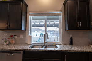 Kitchen featuring backsplash, light stone counters, dark brown cabinets, sink, and dishwasher