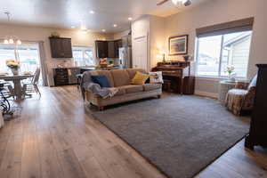 Living room featuring ceiling fan with notable chandelier, light wood-type flooring, and a wealth of natural light