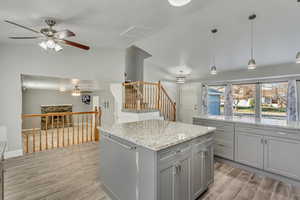 Kitchen with gray cabinetry, tile flooring, decorative light fixtures, a kitchen island, and granite counters