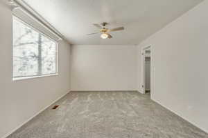 Primary bedroom features a textured ceiling, light-colored carpet, and ceiling fan