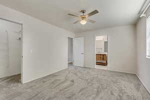 Primary bedroom with light carpet, ensuite bathroom, and ceiling fan