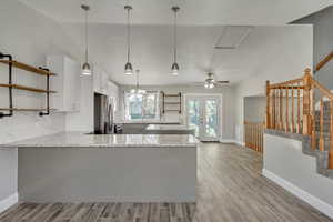 Kitchen featuring kitchen peninsula, vaulted ceiling, stainless steel fridge, granite countertops, and white and gray cabinetry