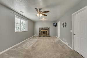 Living room featuring ceiling fan, light colored carpet, a textured ceiling, and a stone fireplace