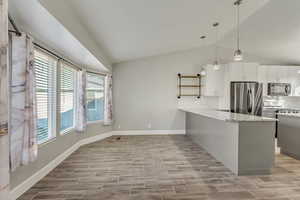 Kitchen with light tile flooring, kitchen peninsula, vaulted ceiling, white and gray cabinets, and appliances with stainless steel finishes