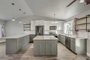 Kitchen featuring vaulted ceiling, ceiling fan with notable chandelier, hanging light fixtures, gray cabinets, and stainless steel appliances