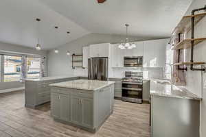 Kitchen featuring decorative light fixtures, a kitchen island, stainless steel appliances, and vaulted ceiling