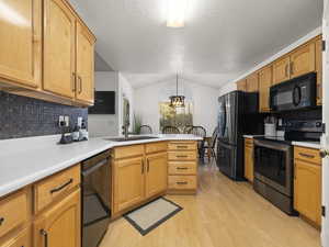 Kitchen with light hardwood / wood-style flooring, kitchen peninsula, decorative light fixtures, vaulted ceiling, and black appliances