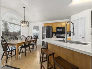 Kitchen featuring decorative backsplash, decorative light fixtures, fridge with ice dispenser, light hardwood / wood-style floors, and lofted ceiling