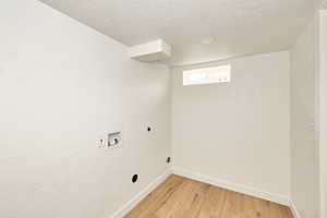 Laundry area with hookup for an electric dryer, hookup for a washing machine, a textured ceiling, and light hardwood / wood-style flooring