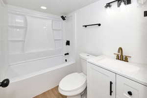 Full bathroom featuring hardwood / wood-style floors, a textured ceiling, toilet, shower / washtub combination, and vanity