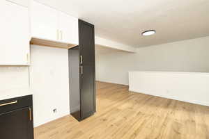 Kitchen featuring a textured ceiling, light hardwood / wood-style floors, white cabinetry, and tasteful backsplash