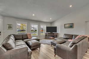 Living room featuring a textured ceiling, high vaulted ceiling, and light hardwood / wood-style flooring