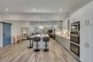 Kitchen with a barn door, light wood-type flooring, appliances with stainless steel finishes, a kitchen island, and white cabinetry