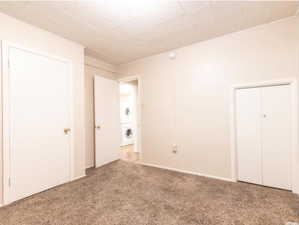 Unfurnished bedroom with light carpet and stacked washer and clothes dryer