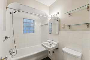 Full bathroom with sink, tiled shower / bath combo, tile walls, and toilet