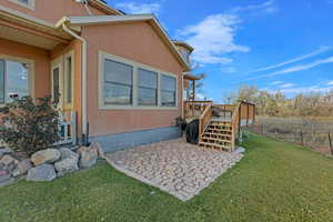 View of property exterior featuring a lawn, a patio, and a wooden deck