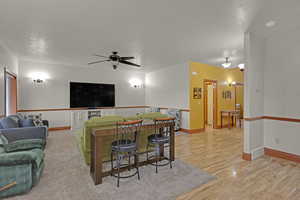 Living room with ceiling fan, a textured ceiling, and light hardwood / wood-style flooring