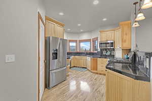 Kitchen featuring light brown cabinetry, stainless steel appliances, hanging light fixtures, and light hardwood / wood-style flooring