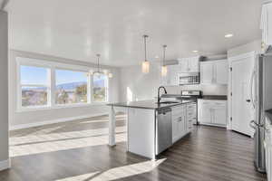 Kitchen featuring appliances with stainless steel finishes, decorative light fixtures, an island with sink, and white cabinets