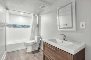 Full bathroom featuring wood-type flooring, vanity, a textured ceiling, shower / bath combo, and toilet