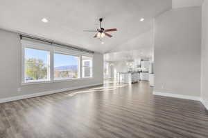 Unfurnished living room with ceiling fan with notable chandelier, dark wood-type flooring, a textured ceiling, high vaulted ceiling, and a mountain view