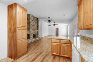 Kitchen with a stone fireplace, light stone counters, kitchen peninsula, white dishwasher, and light wood-type flooring