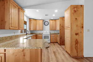 Kitchen with kitchen peninsula, white electric range, light brown cabinetry, and lofted ceiling