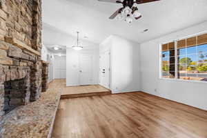 Unfurnished living room with a textured ceiling, ceiling fan, a fireplace, and light hardwood / wood-style flooring