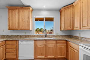 Kitchen with white dishwasher, light stone counters, and sink