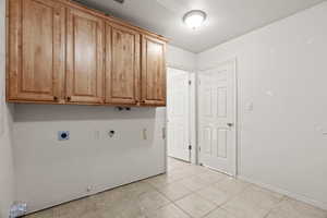 Clothes washing area featuring electric dryer hookup, cabinets, gas dryer hookup, hookup for a washing machine, and light tile patterned flooring