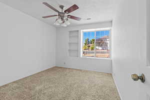 Carpeted empty room featuring ceiling fan and a textured ceiling