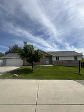 View of front of home with a front lawn, driveway, brick siding, and a garage