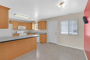 Kitchen featuring a textured ceiling, kitchen peninsula, sink, and white appliances