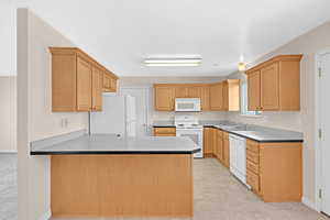 Kitchen with sink, white appliances, kitchen peninsula, and light brown cabinetry