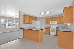 Kitchen with kitchen peninsula, a textured ceiling, white appliances, light colored carpet, and sink