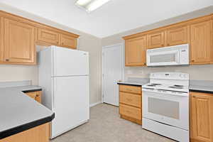 Kitchen with light brown cabinetry and white appliances