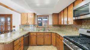 Kitchen with sink, backsplash, kitchen peninsula, light tile patterned flooring, and appliances with stainless steel finishes