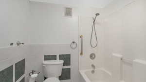 Bathroom featuring bathtub / shower combination, tile walls, and toilet