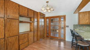 Kitchen with light wood-type flooring, tasteful backsplash, a textured ceiling, pendant lighting, and a notable chandelier