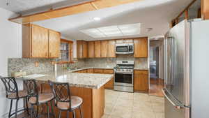 Kitchen with a breakfast bar, kitchen peninsula, stainless steel appliances, and tasteful backsplash