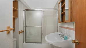 Bathroom with combined bath / shower with glass door, toilet, and backsplash