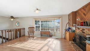 Sitting room with a fireplace, a textured ceiling, light wood-type flooring, and ceiling fan