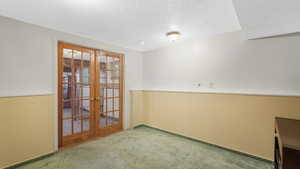 Empty room featuring carpet flooring, french doors, and a textured ceiling