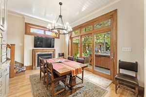 Dining room featuring crown molding, a premium fireplace, a notable chandelier, and light wood-type flooring