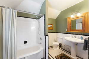 Bathroom featuring tile patterned floors, lofted ceiling, toilet, shower / tub combo with curtain, and tile walls